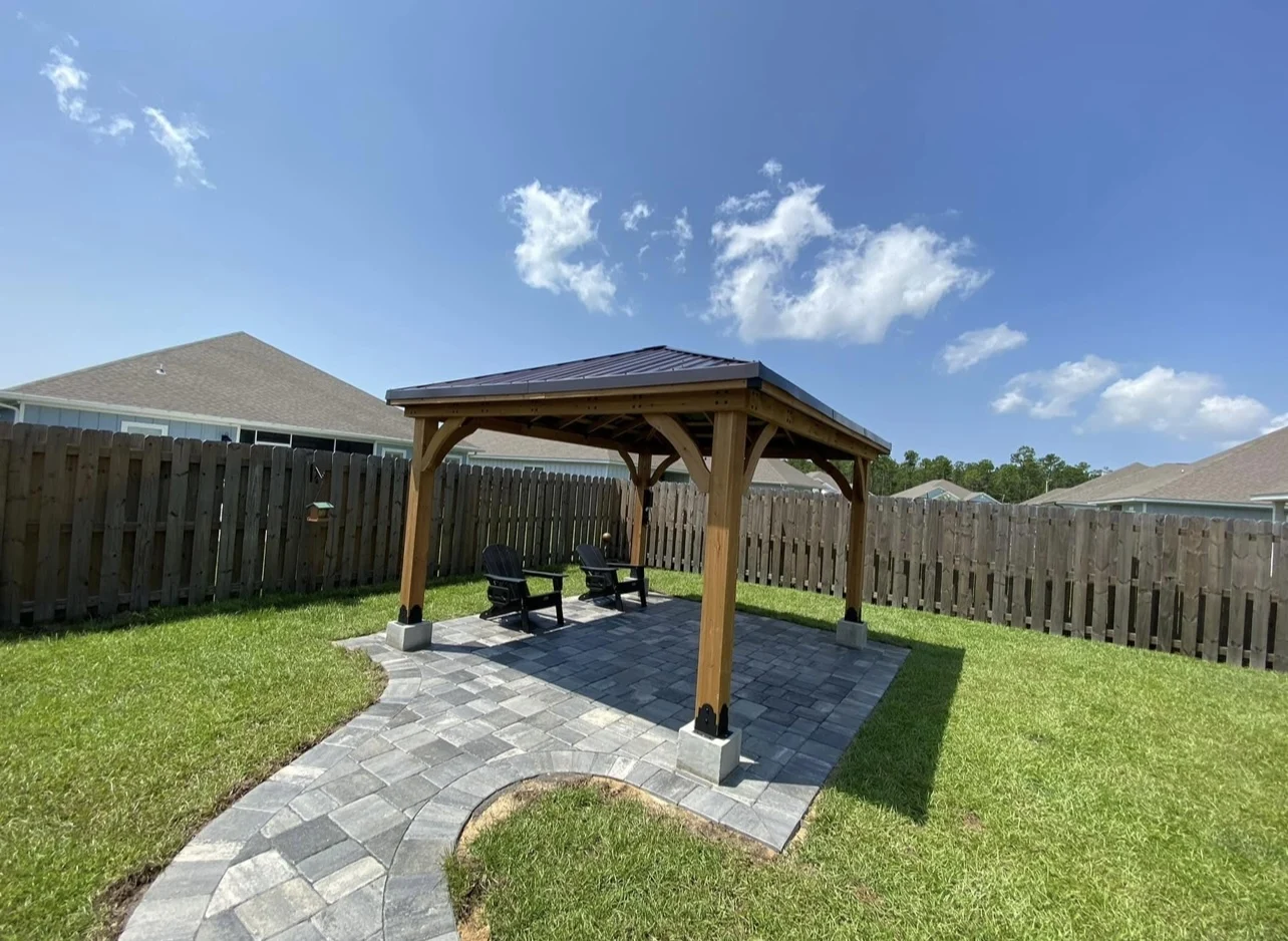 Wood pavilion set on a paver patio with anchored posts in a Pensacola backyard